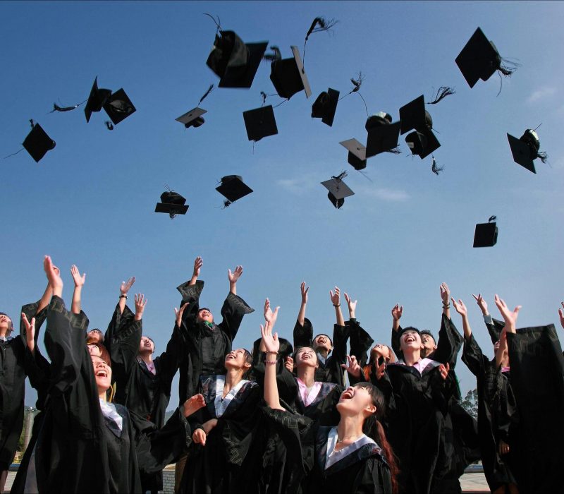Group of graduates celebrating by throwing caps in the air during a sunny day.